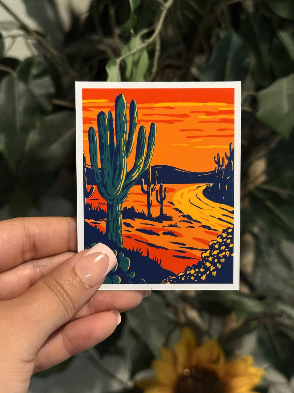 Hand holding a berry medium photo magnet with a desert landscape design featuring cacti.