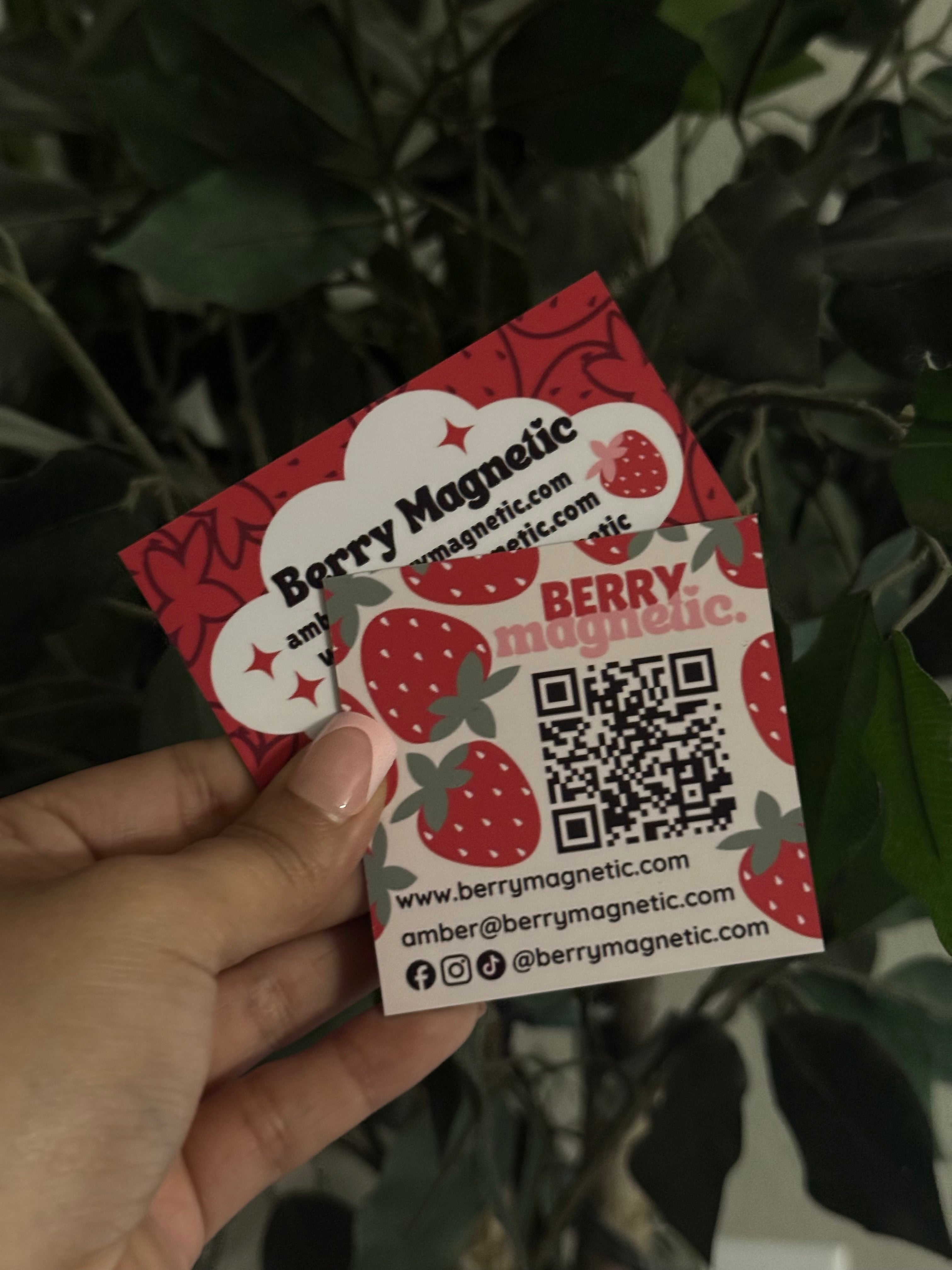 Hand holding both a square with a QR code and standard Berry Magnetic business card against a leafy background