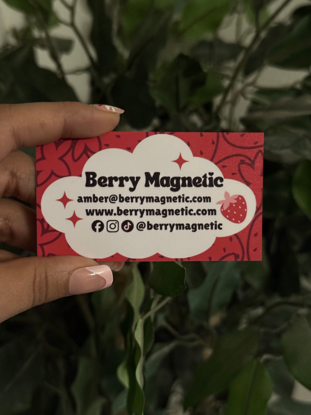 Hand holding a Berry Magnetic business card with a red and white design.